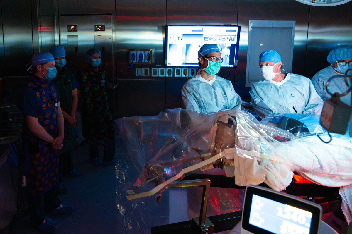 Students in scrubs, caps and masks watch a surgery from inside the operating room